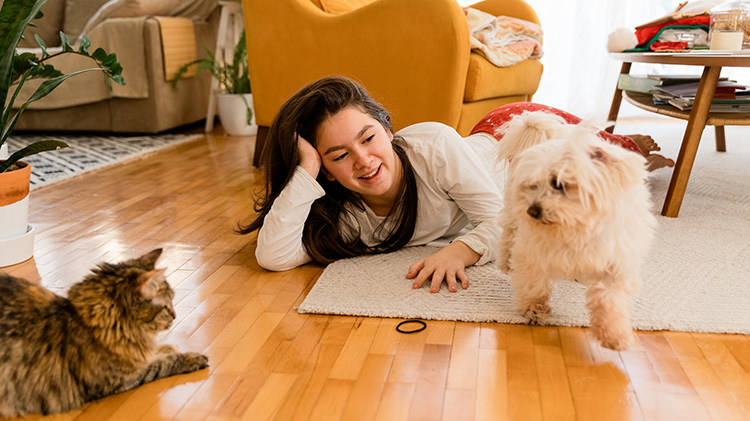 Una joven está acostada en el piso de la sala jugando con su gato y su perro.