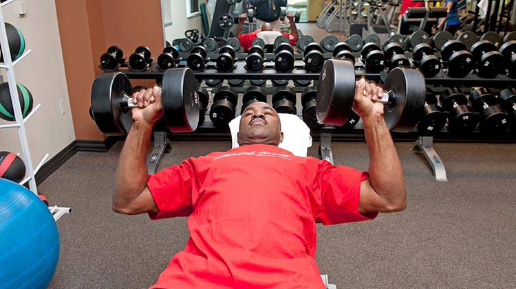 Usando los beneficios de su compañía, un hombre levanta pesas en el gimnasio.