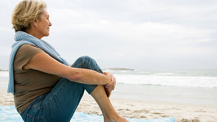 Mujer sentada en una manta en la playa mirando hacia el agua.