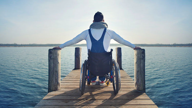 Hombre con incapacidad sentado en su silla de ruedas mirando un lago desde un embarcadero