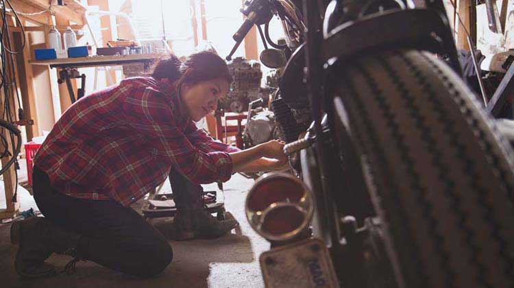 Una mujer arreglando una moto en un garaje.