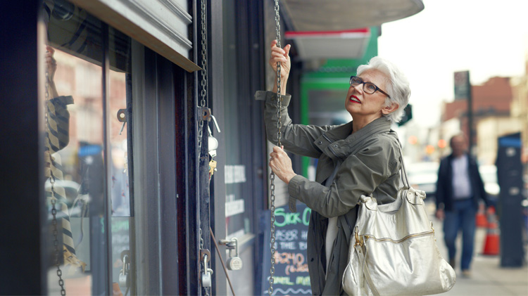 Una mujer abre la persiana de seguridad de su negocio.
