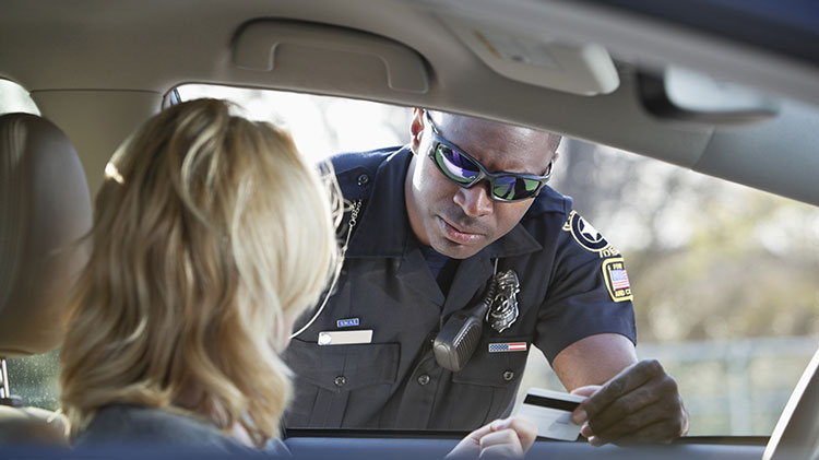 A una mujer joven en su carro la ha parado la policía que habla con ella mientras le da la licencia de manejo.