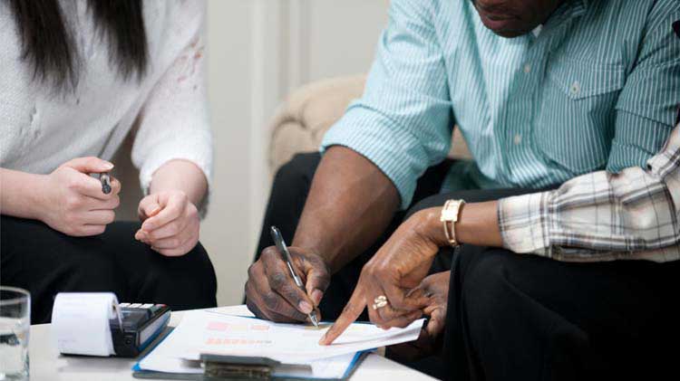 Una pareja sentada firmando papeles de un contrato de arrendamiento.