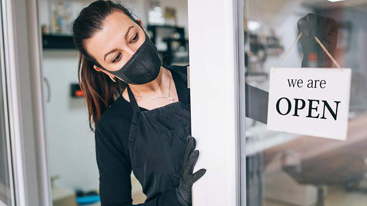 Una mujer usa una máscara facial mientras abre su negocio.