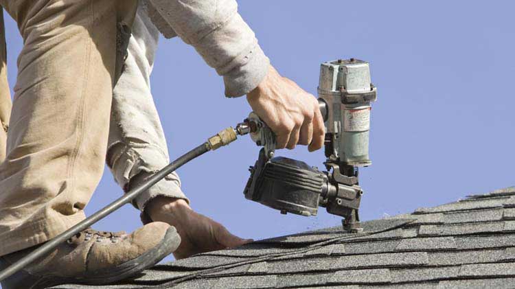 Un hombre en el techo arreglando tejas.