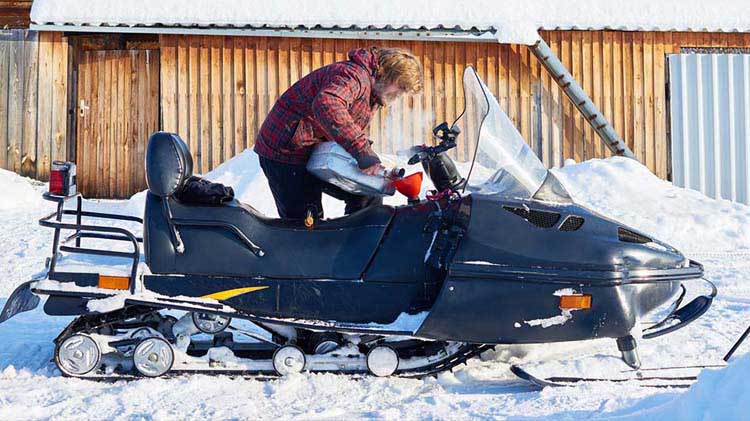 Hombre de pie, poniendo combustible a su moto de nieve
