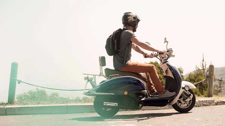 Un hombre con un casco montando una motoneta.
