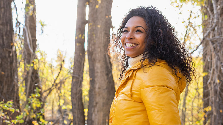 Smiling woman wearing a yellow jacket in the woods.