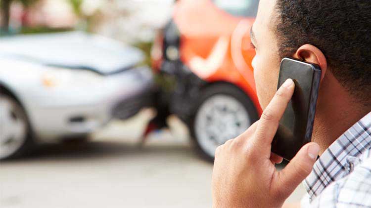 Un hombre en el teléfono informando de un carro declarado pérdida total.