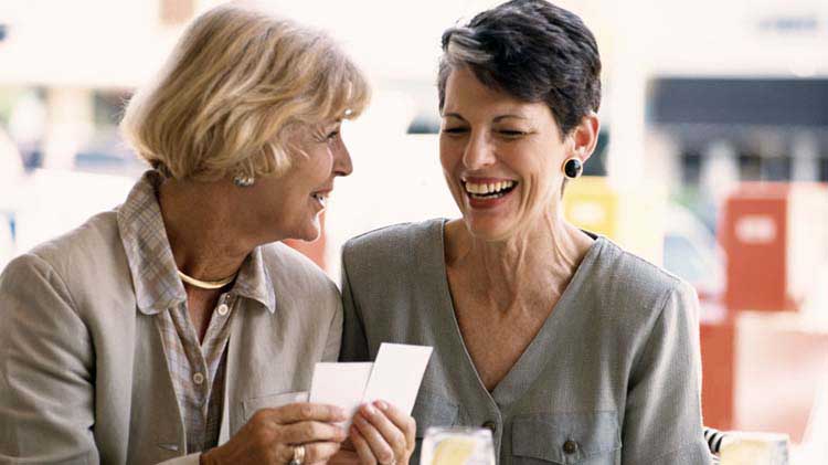 Dos mujeres mayores teniendo una conversación feliz mientras miran las tarjetas.