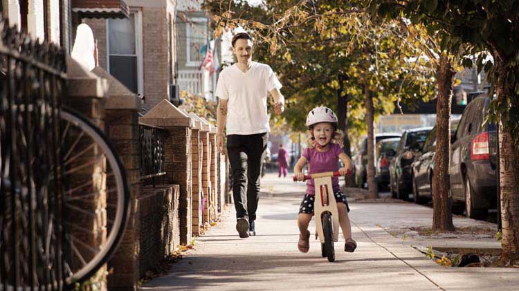 Padre viendo a su hija pequeña andar en una bicicleta y considerando la importancia del seguro de vida.