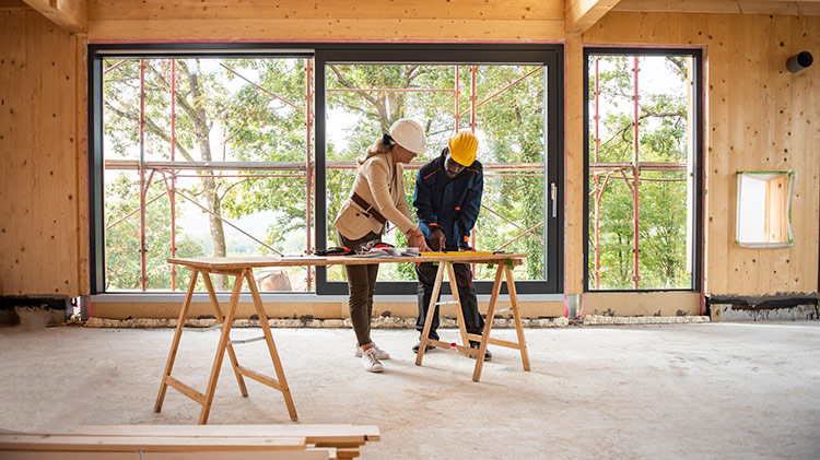 Un hombre y una mujer con cascos de seguridad revisan planos de construcción en interiores en un sitio de trabajo.