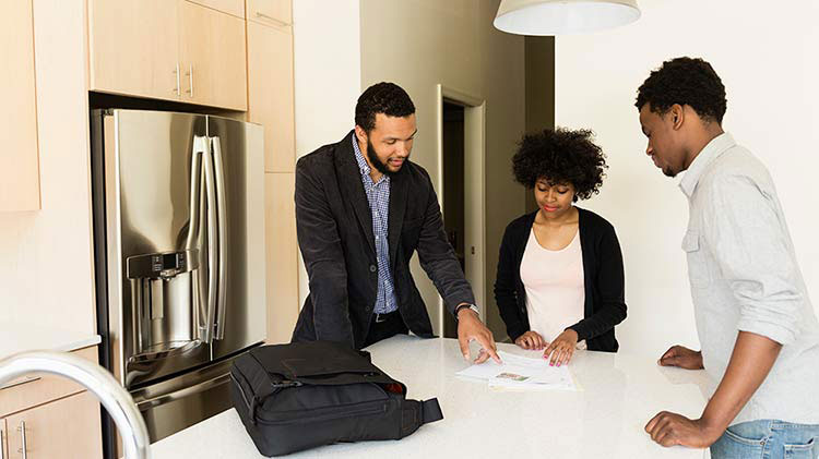 Un arrendador les enseña a dos inquilinos el contrato de una casa.