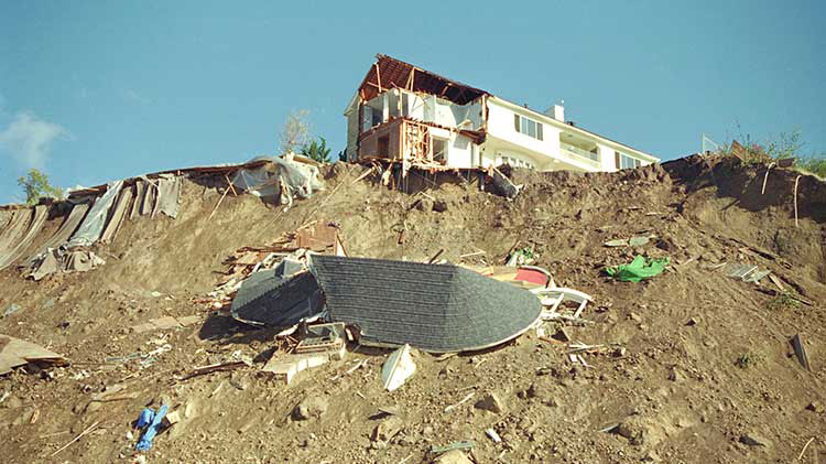 Una casa dañada por un terremoto en una colina cubierta de escombros.