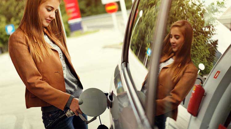 Mujer joven pone gasolina a su carro en una estación de combustible.