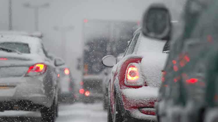 Carros con nieve en ellos, en tráfico y está nevando.