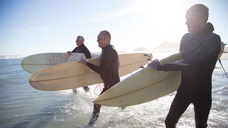 Tres hombres retirados están entrando al océano para surfear.