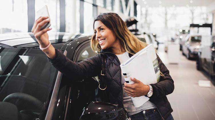 Mujer tomándose una foto con la compra de su auto nuevo.
