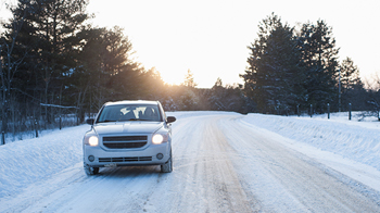 Un sedán blanco conduciendo en una carretera cubierta de nieve.
