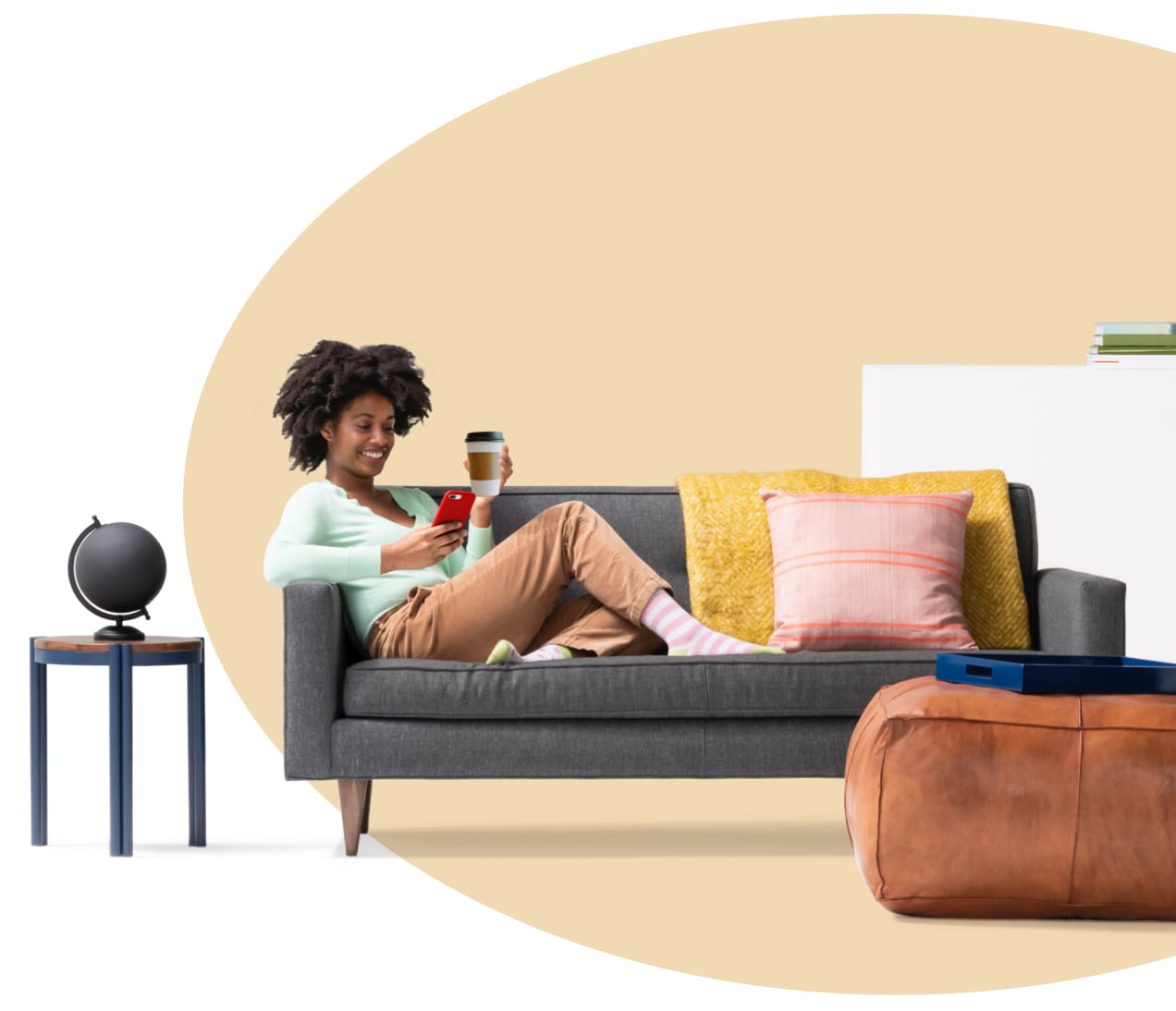 Mujer sentada en un sillón sosteniendo una taza de café y leyendo en su iPhone lo que cubre el seguro de inquilinos. Hay un globo terráqueo en la mesita.